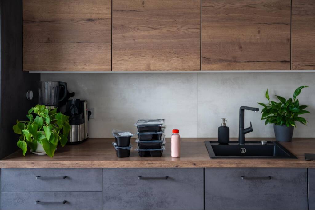 Black meal boxes on top of a stained wooden counter near the sink and under stained kitchen cabinets.