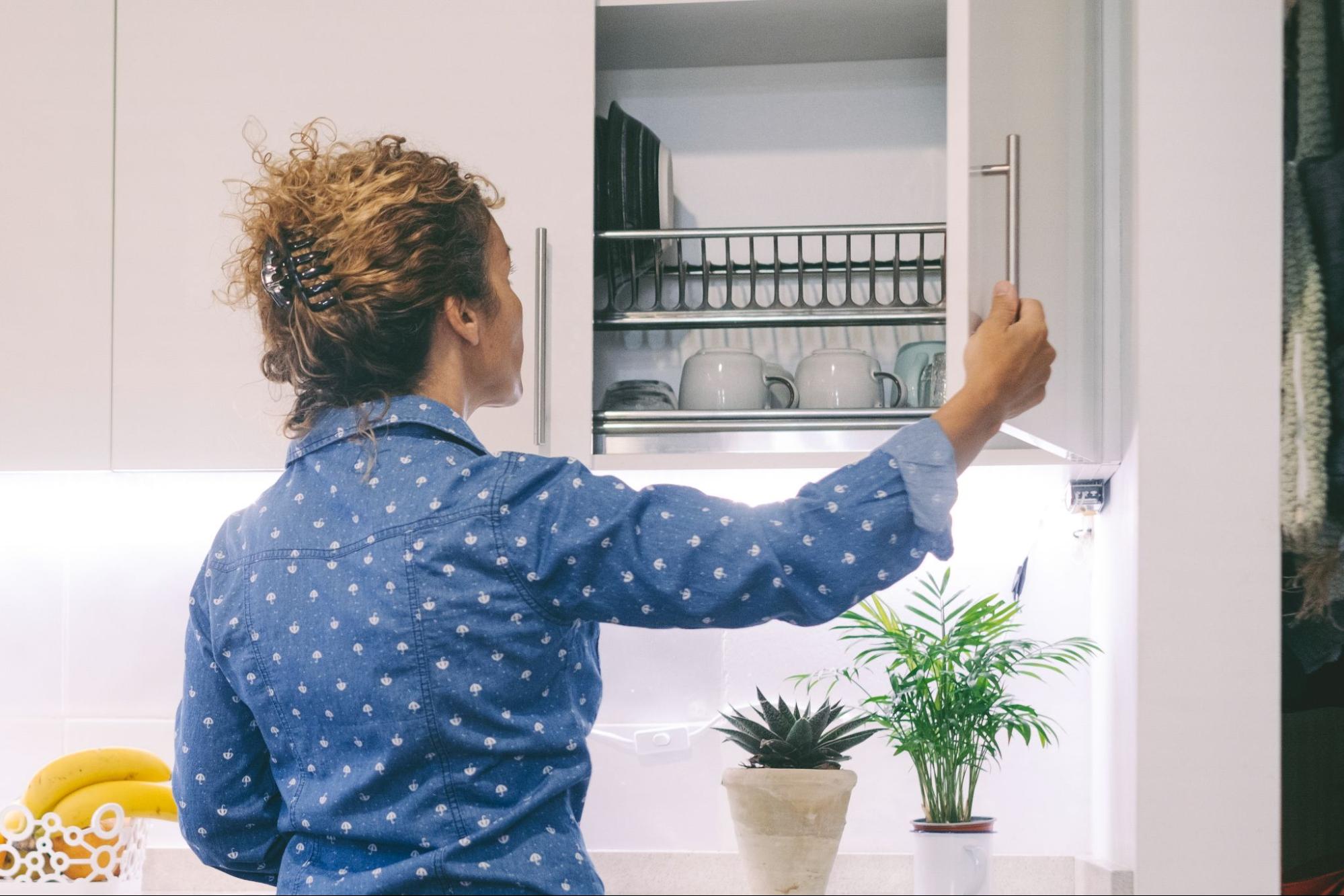 A woman opens a hanging kitchen cabinet with well-adjusted hinges to grab a coffee cup.