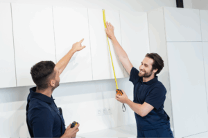 Two workers measuring cabinets.