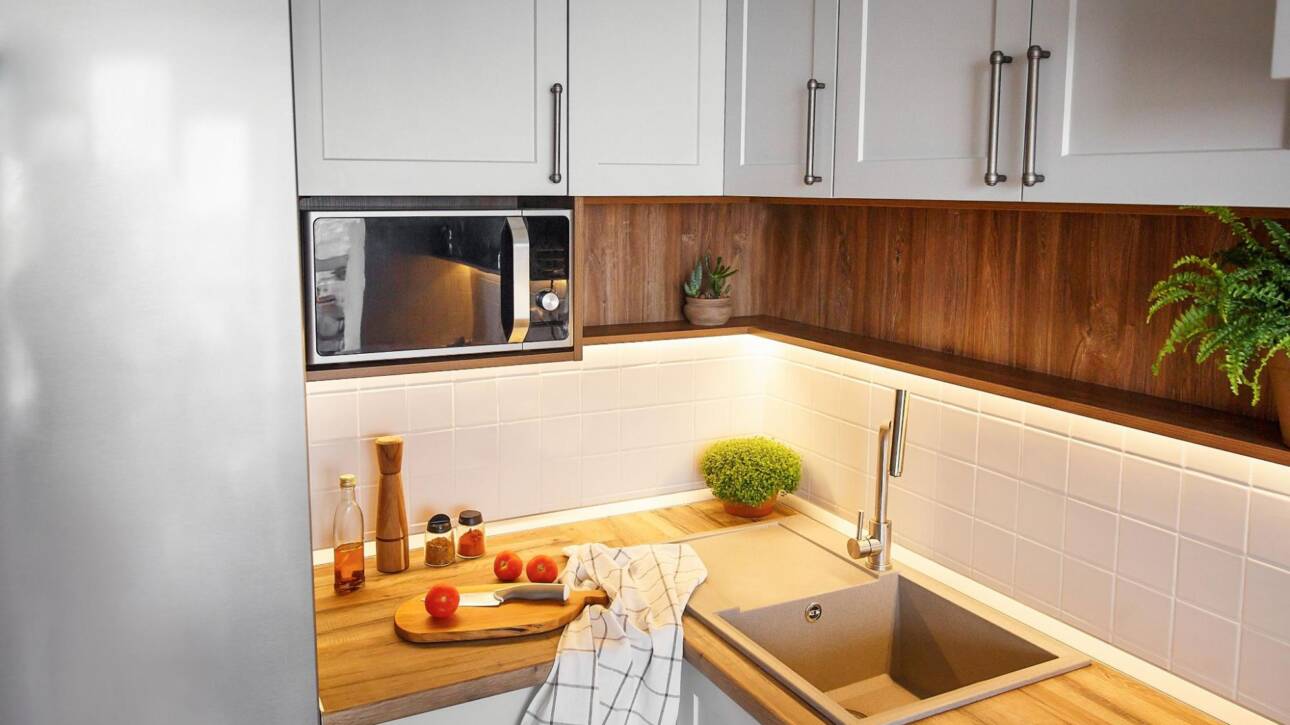 Modern wood corner cabinets next to a microwave, fridge, and sink.