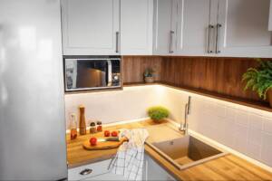 Modern wood corner cabinets next to a microwave, fridge, and sink.
