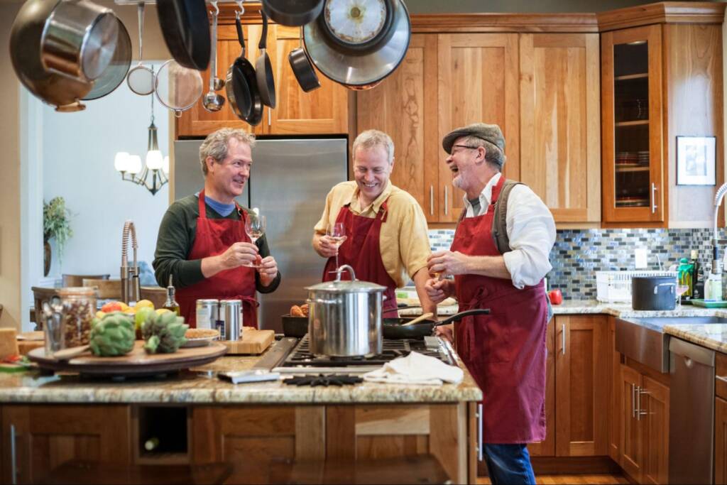 Three senior men friends having fun while cooking a meal in a cozy kitchen with beautifully crafted Amish kitchen cabinets.