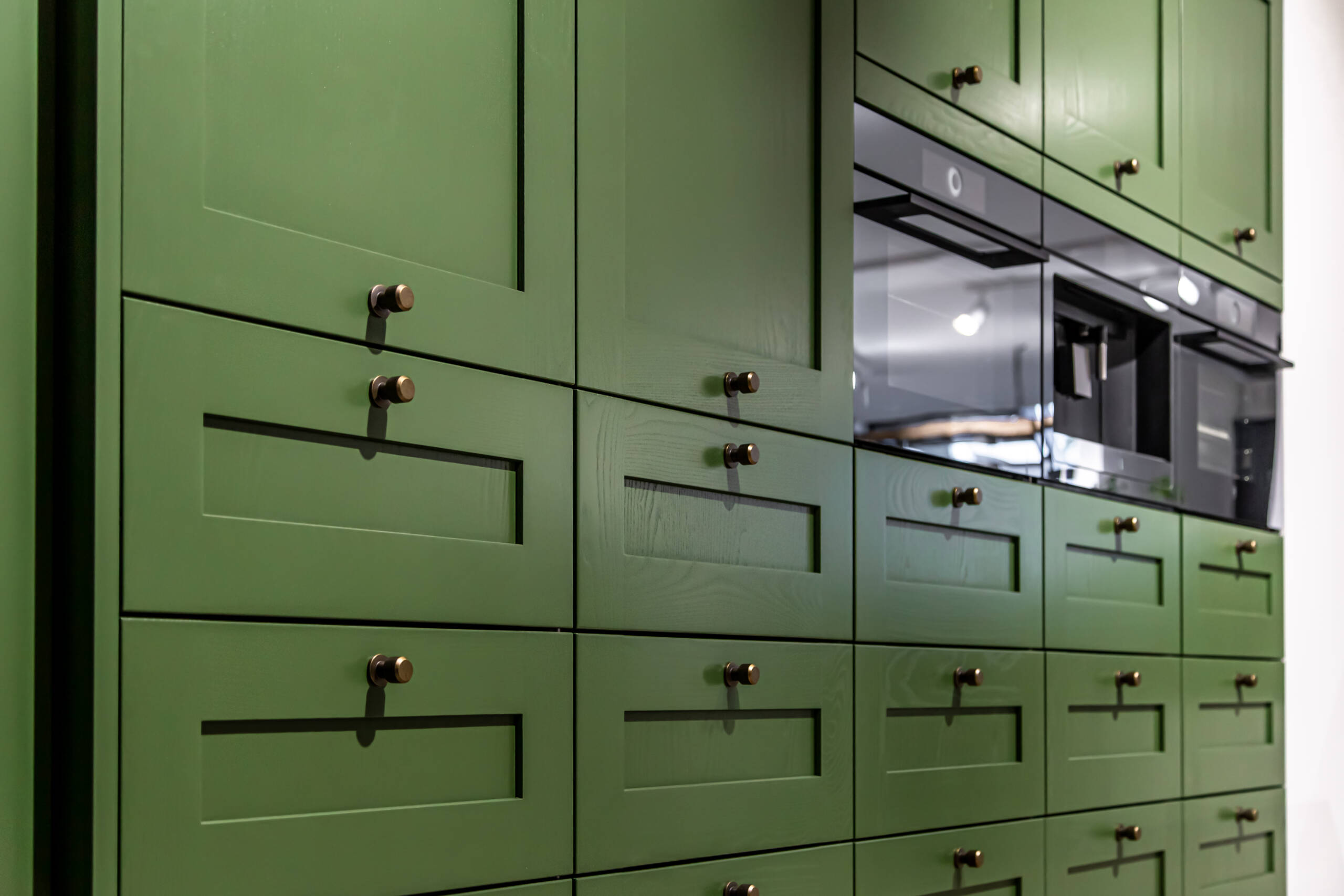 Closeup on a wall of green shaker cabinets in a kitchen.