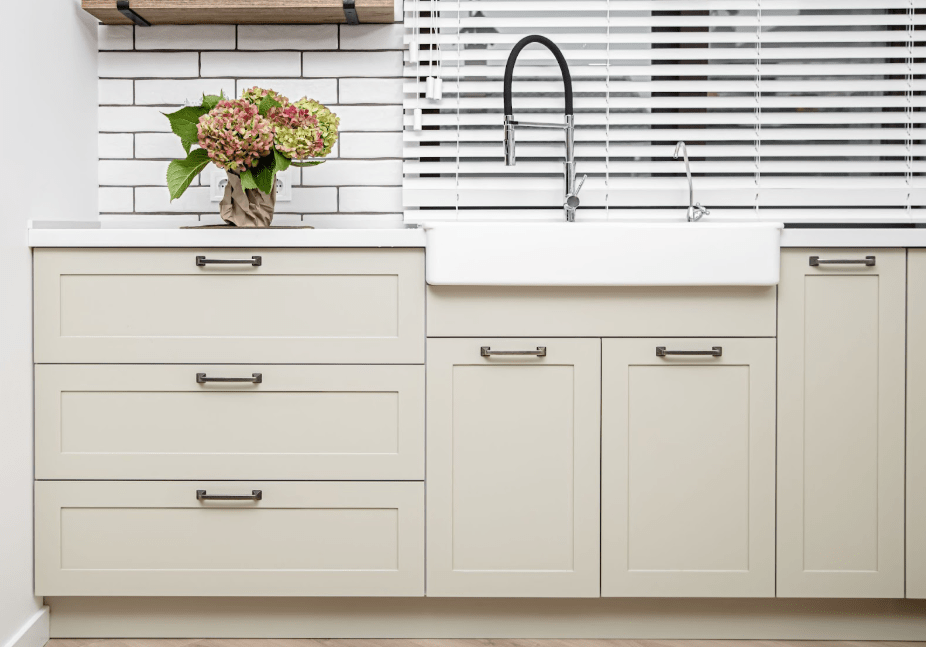 A close-up of beige kitchen cabinets under the washbasin, adorned with a pot of flowers, showcasing a minimalist style with clean lines and simplicity.