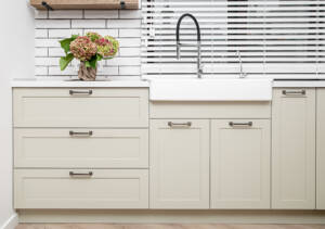 A kitchen sink outfitted with cream shaker cabinets for storage.